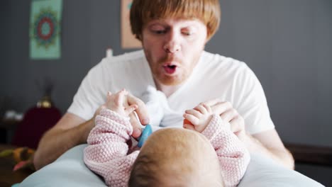 Playful-dad-grimacing-and-soothing-baby-daughter-with-toy